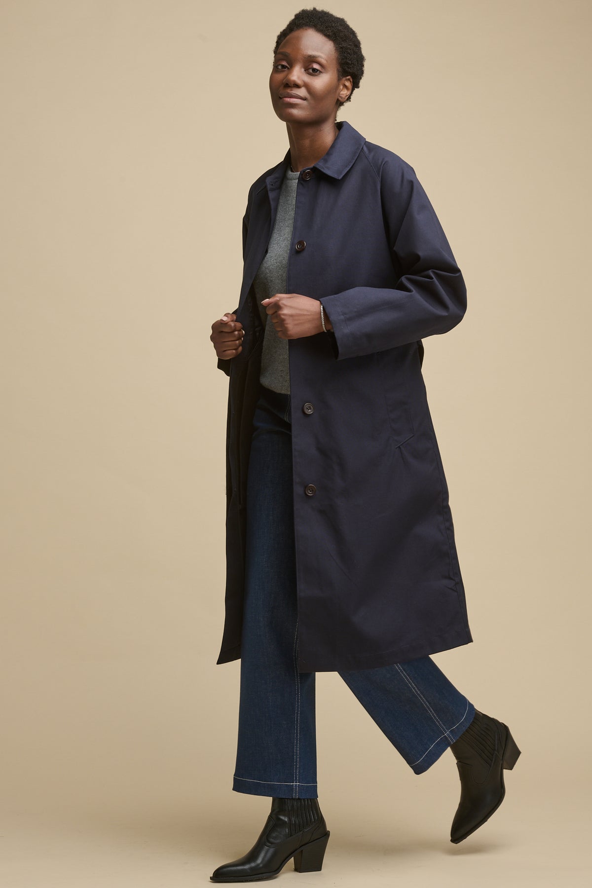full body image of the side of female wearing women's Frances Raglan Belted Raincoat in navy with blue jeans