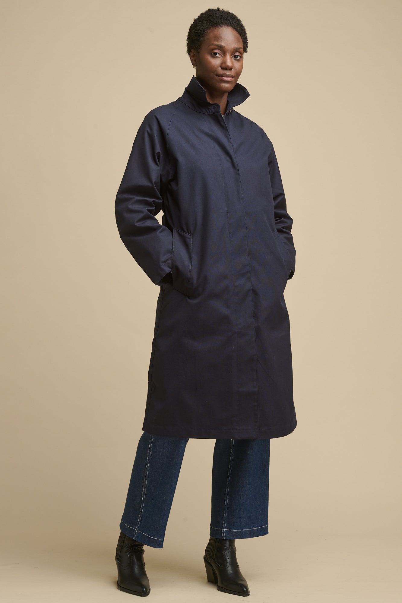 Full body image of female wearing women's Frances Raglan Belted Raincoat in navy with hands in two front pockets
