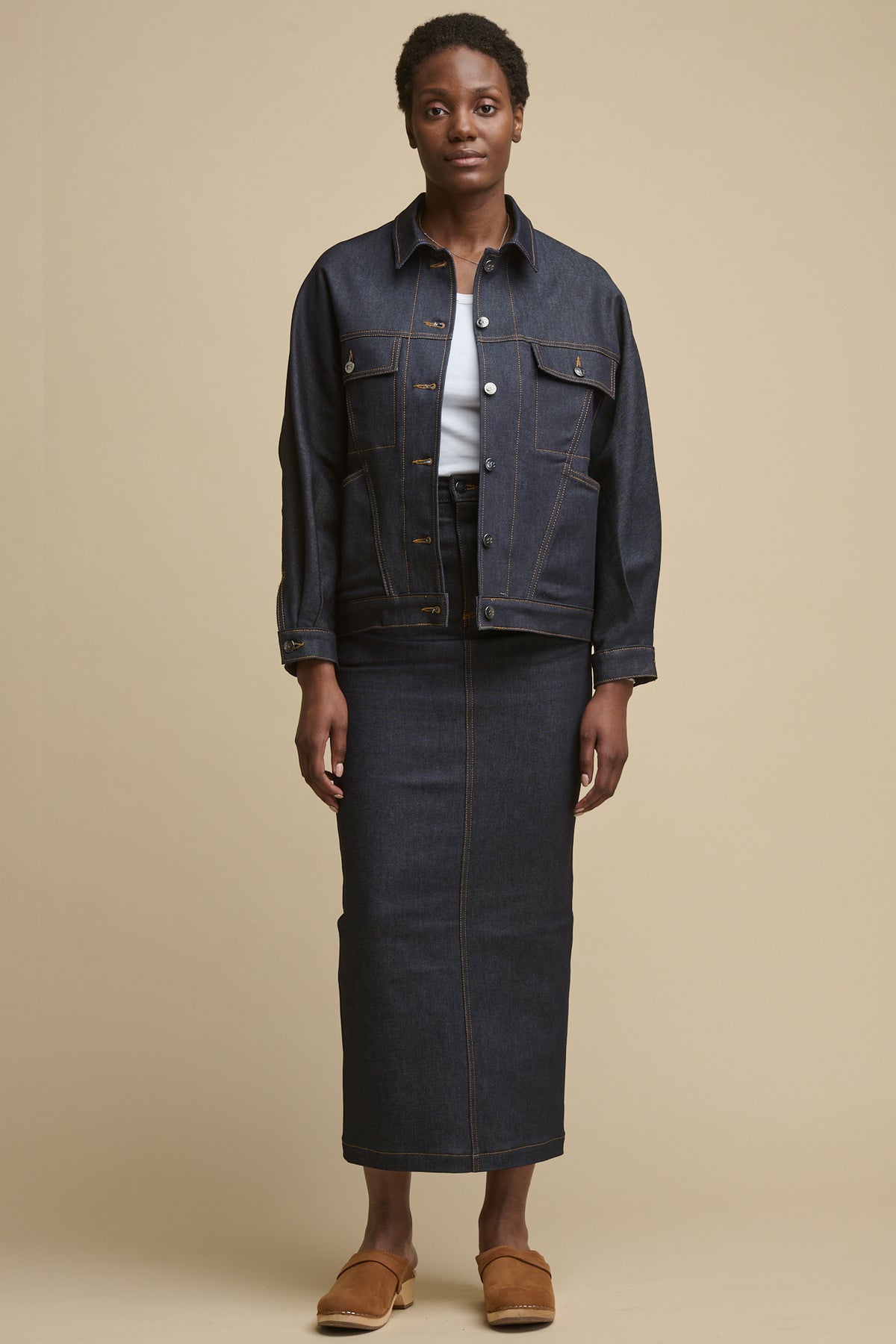 Full body image of black female wearing Frankie denim maxi skirt in indigo with the matching denim jacket, over racer back vest in white