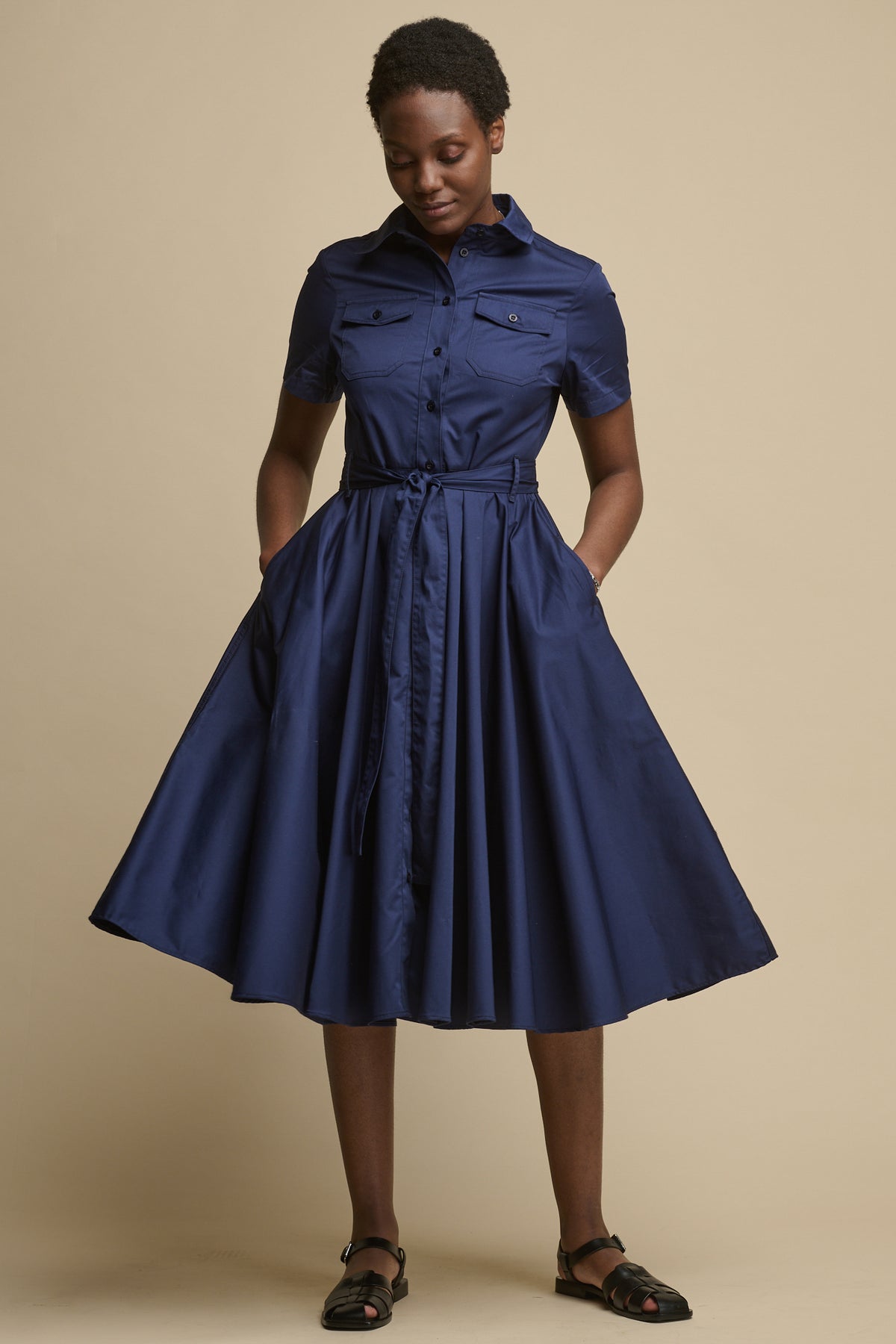 Full body image of the front of female with hands in the front pockets of full skirted phoebe trench dress in navy