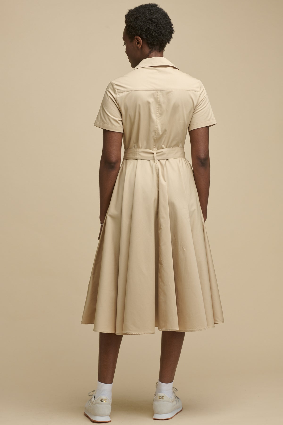 Full body image of the back of female wearing full skirted phoebe trench dress in stone