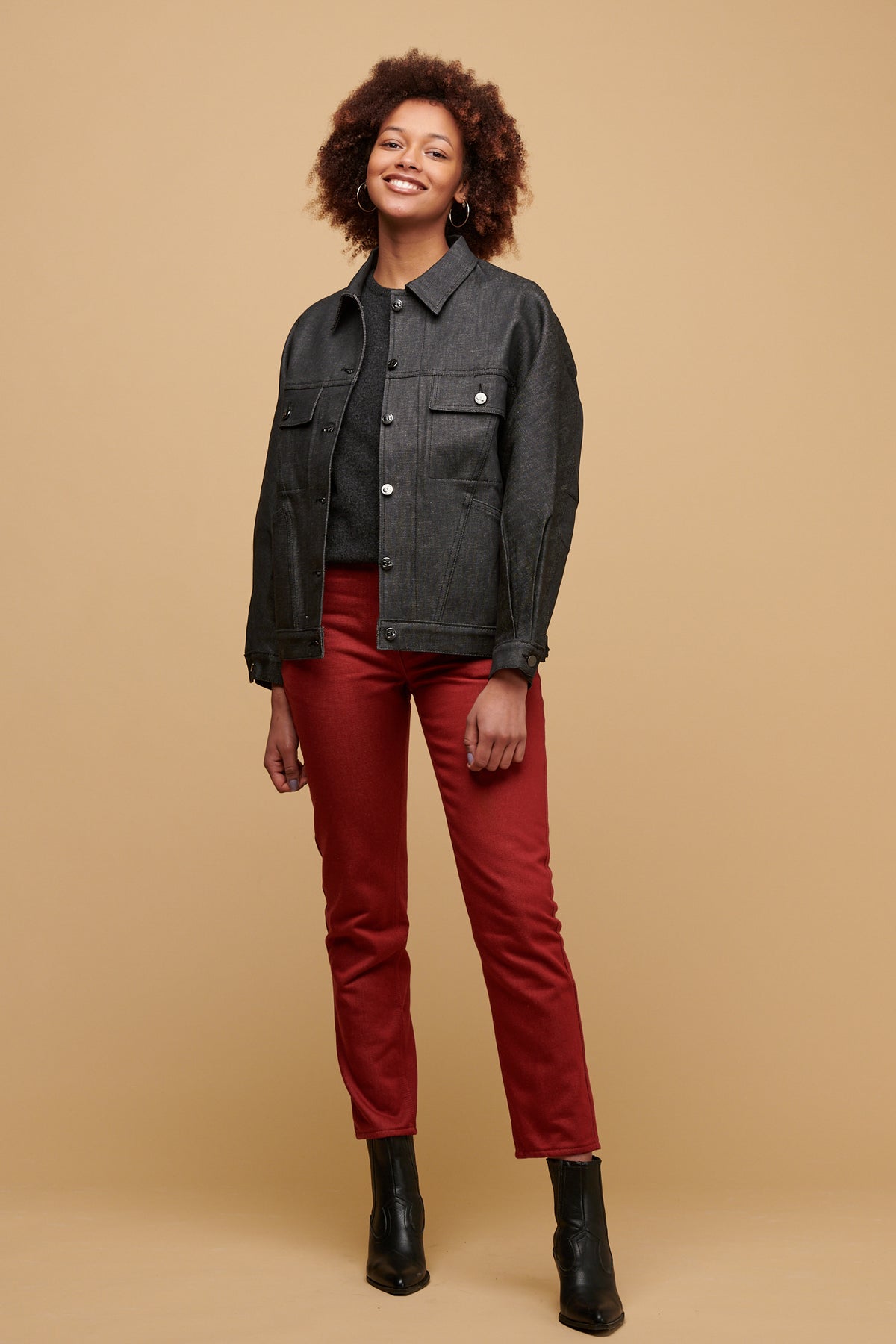 The front of female of colour wearing Gloria jean in burgundy paired with lambswool crew neck in charcoal with Jodie denim jacket over the top and a black boot.