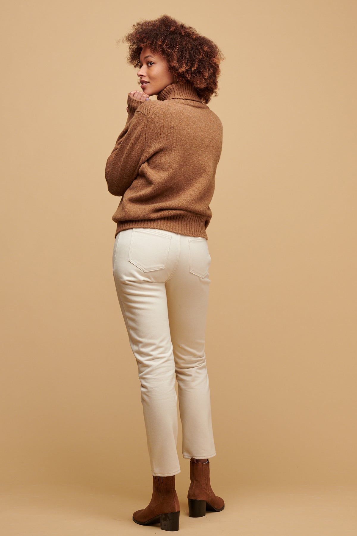 The back of female wearing Gloria jean in ecru paired with dark camel lambswool roll neck and matching suede boots