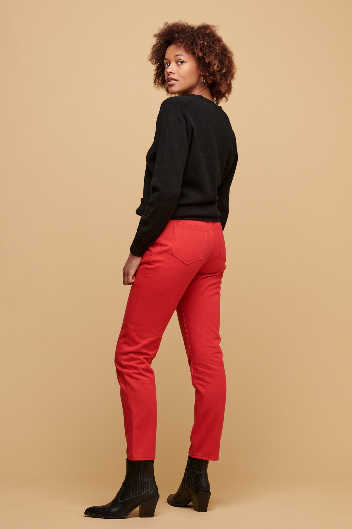 The side of female of colour with her natural afro looking back over her shoulder wearing lambswool cardigan paired with women's Gloria jean in poppy.