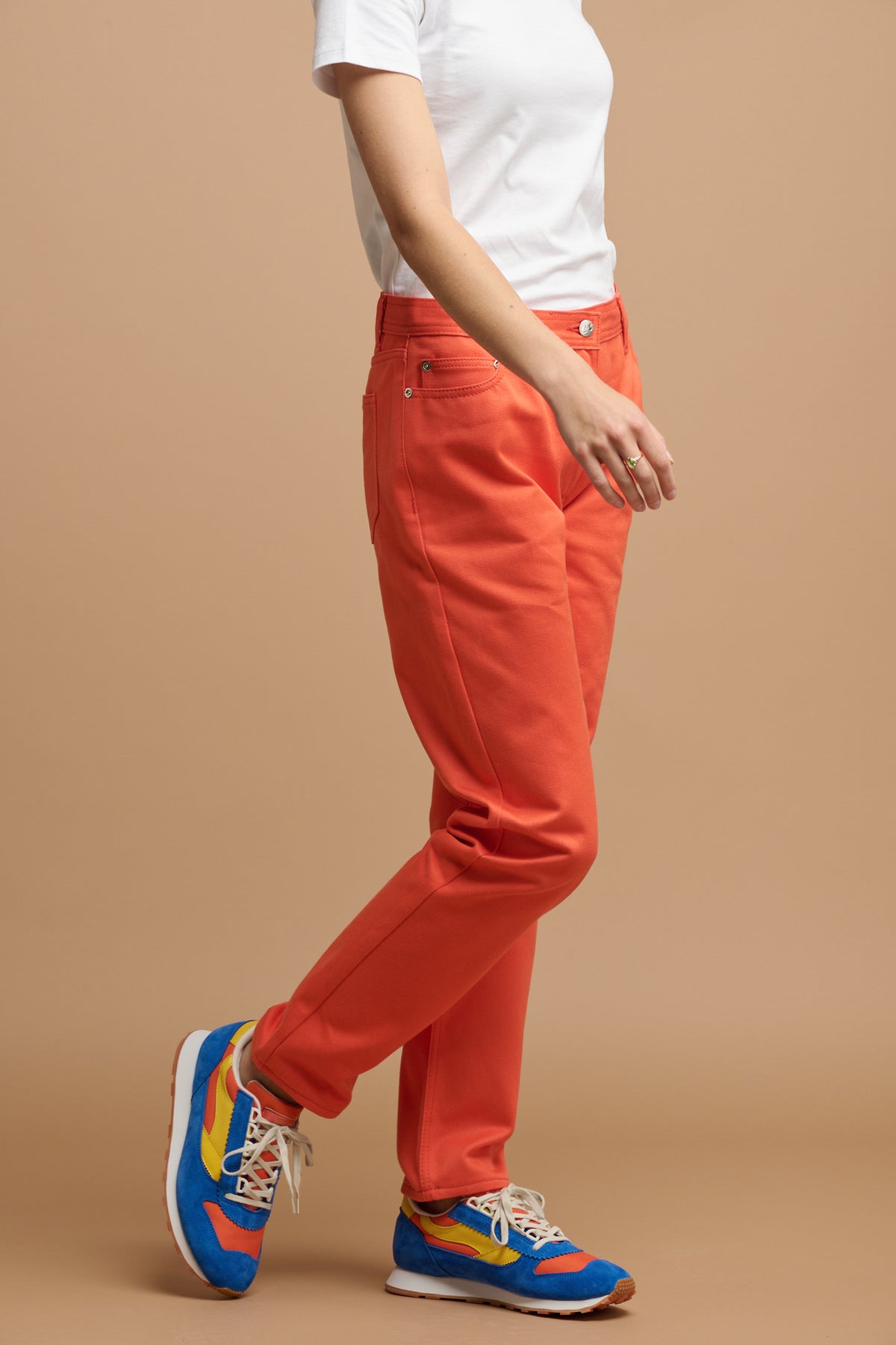 Shoulder down of female wearing Gloria tapered jeans in flame with white t shirt tucked in and Parlick trainers