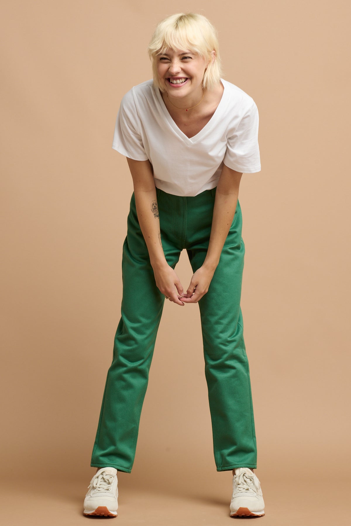 
            Smiley blonde female bending forward wearing Community Clothing Gloria Tapered Jean in green with v neck white t shirt