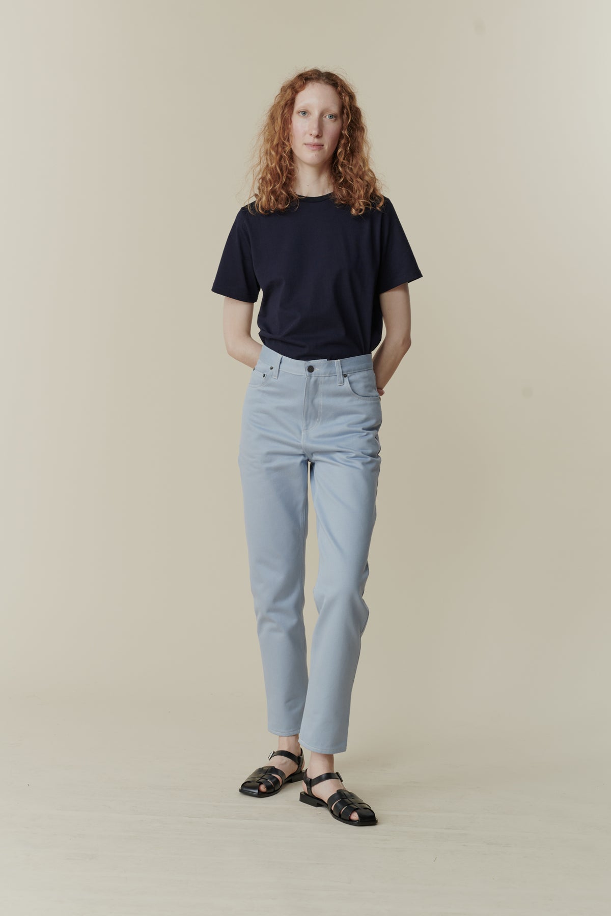 White female with curly ginger shoulder length hair wearing Community Clothing Gloria tapered jeans in light blue paired with navy short sleeve t shirt tucked in