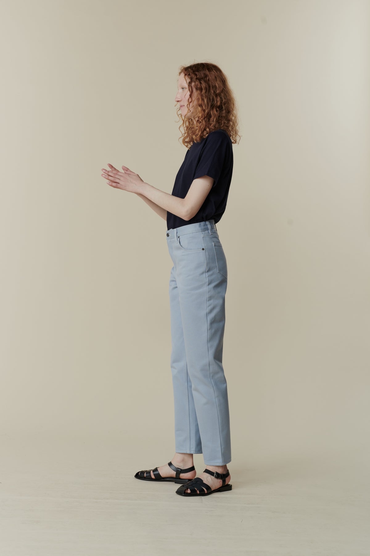 the side of white female with curly ginger shoulder length hair wearing Community Clothing Gloria tapered jeans in light blue paired with navy short sleeve t shirt tucked in