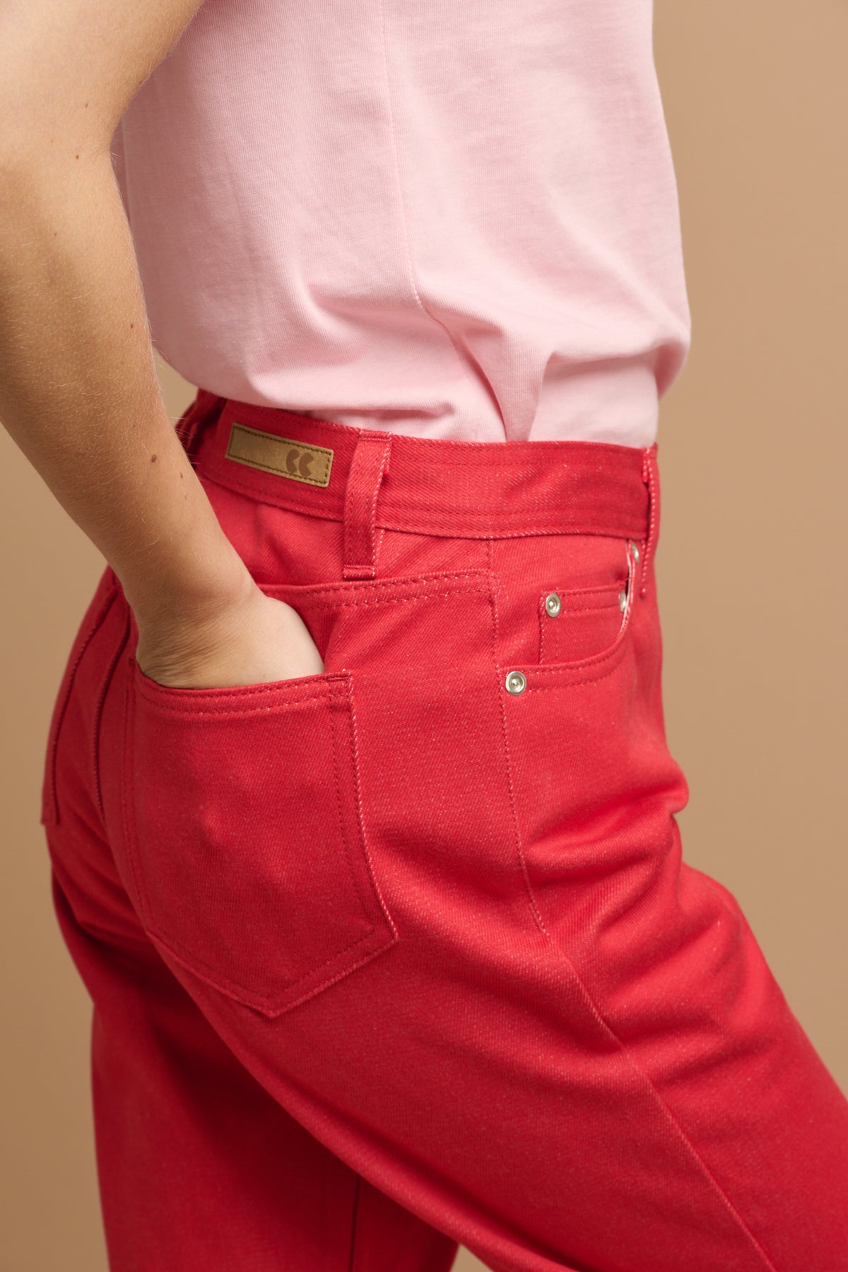 
            Close up female wearing Community Clothing Gloria tapered jeans in poppy red paired with short sleeve t shirt in pink tucked in