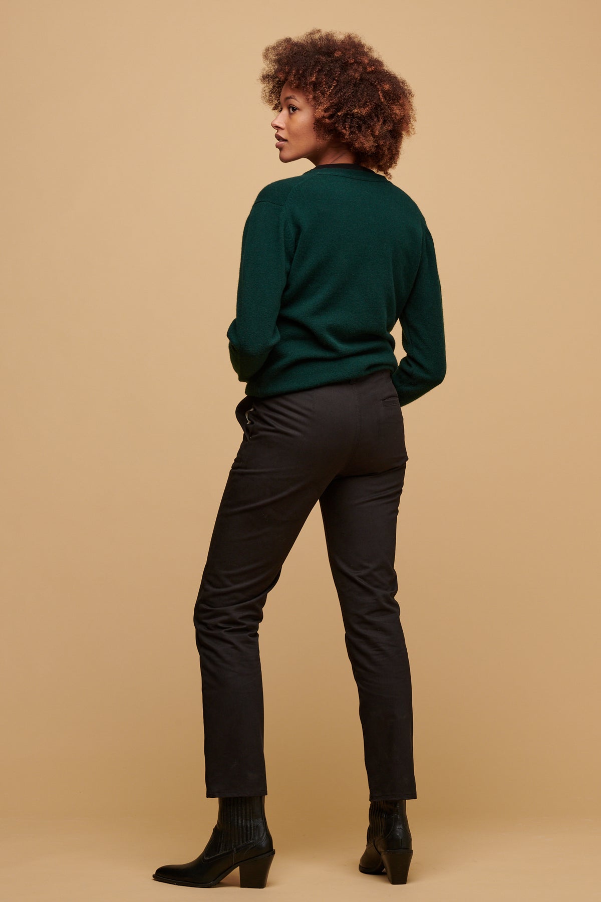 The back of female wearing heavyweight slim chino in black paired with bottle green cardigan and black boots.