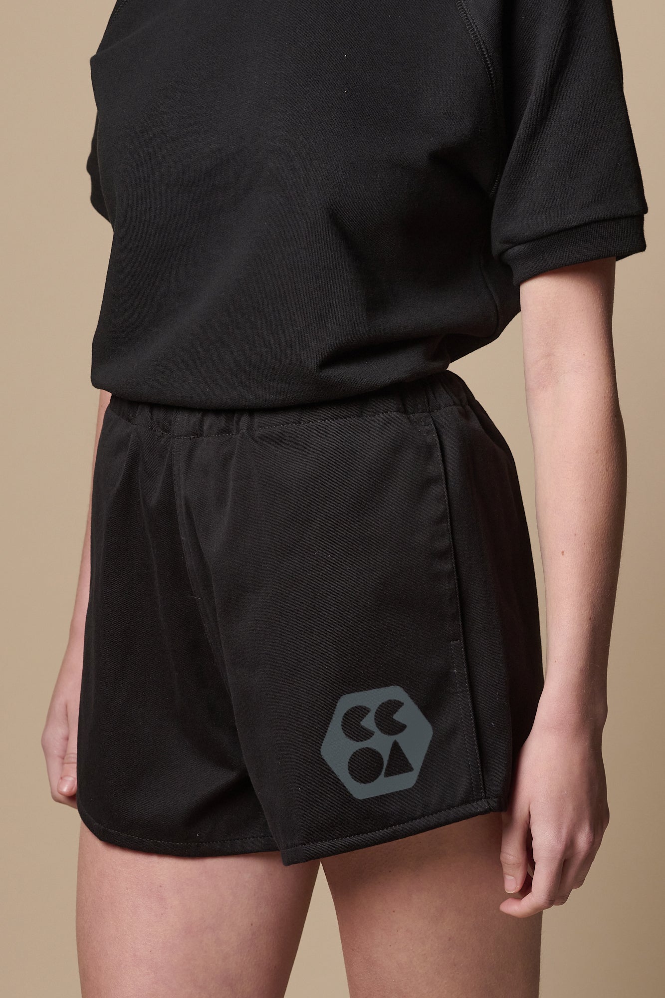 Female wearing heavyweight sports short plastic free in black with CCOA logo on models left leg