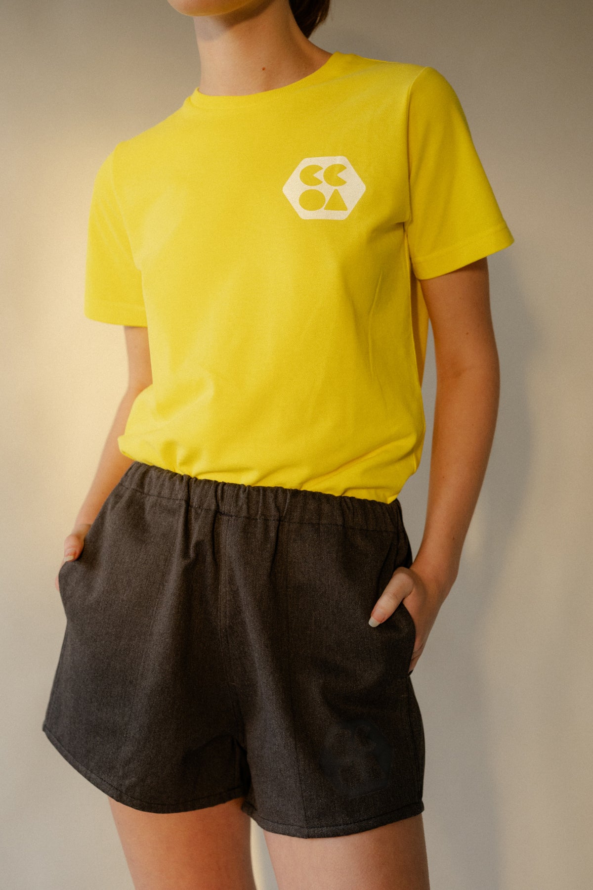 
            Female wearing women&#39;s heavyweight sports short plastic free in charcoal marl with CCOA logo and her hands in front pockets.
