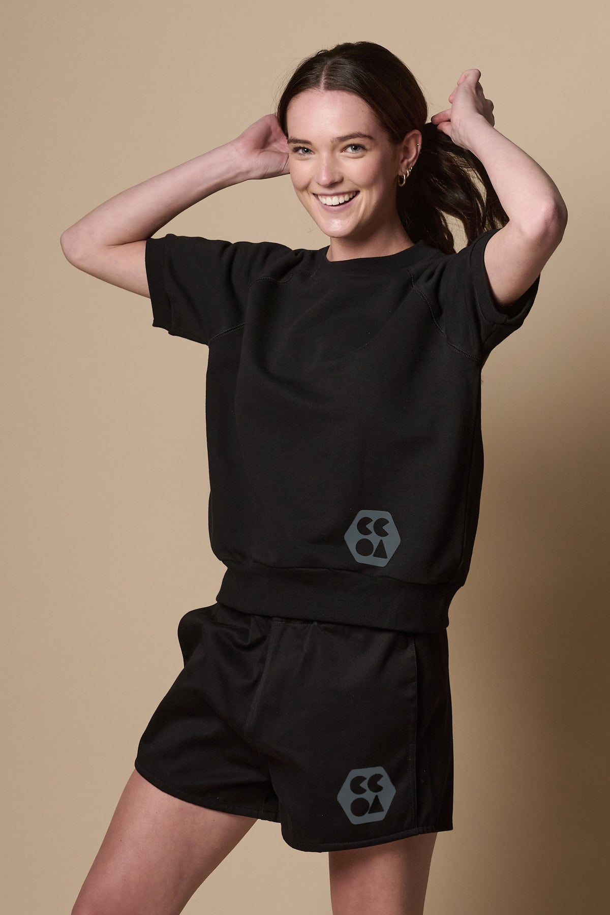 Female wearing heavyweight sports short plastic free in black with CCOA logo on models left leg paired with short sleeve raglan training top in black