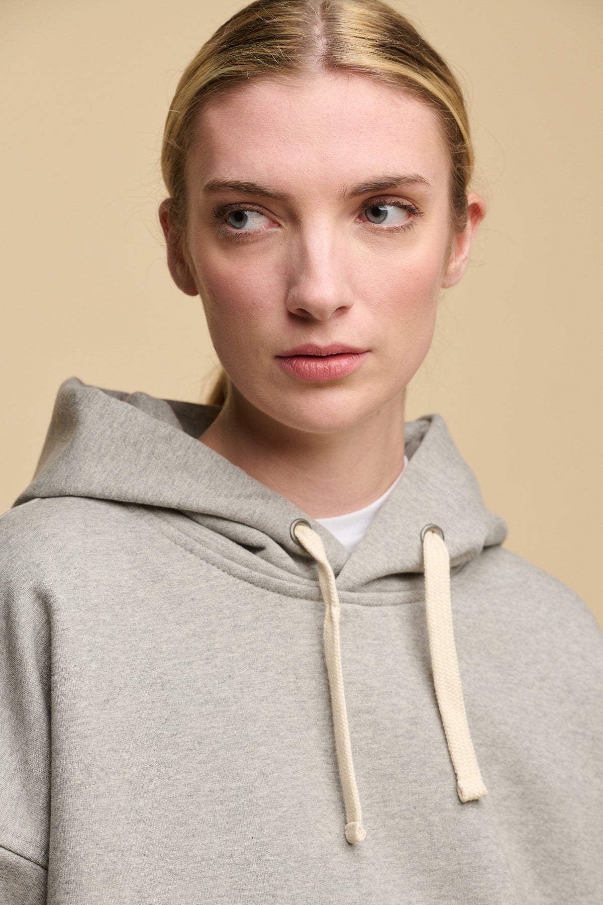 
            Portrait of female wearing heritage hooded sweatshirt in grey worn over crew neck t shirt in white. Ecru drawstring through the hood