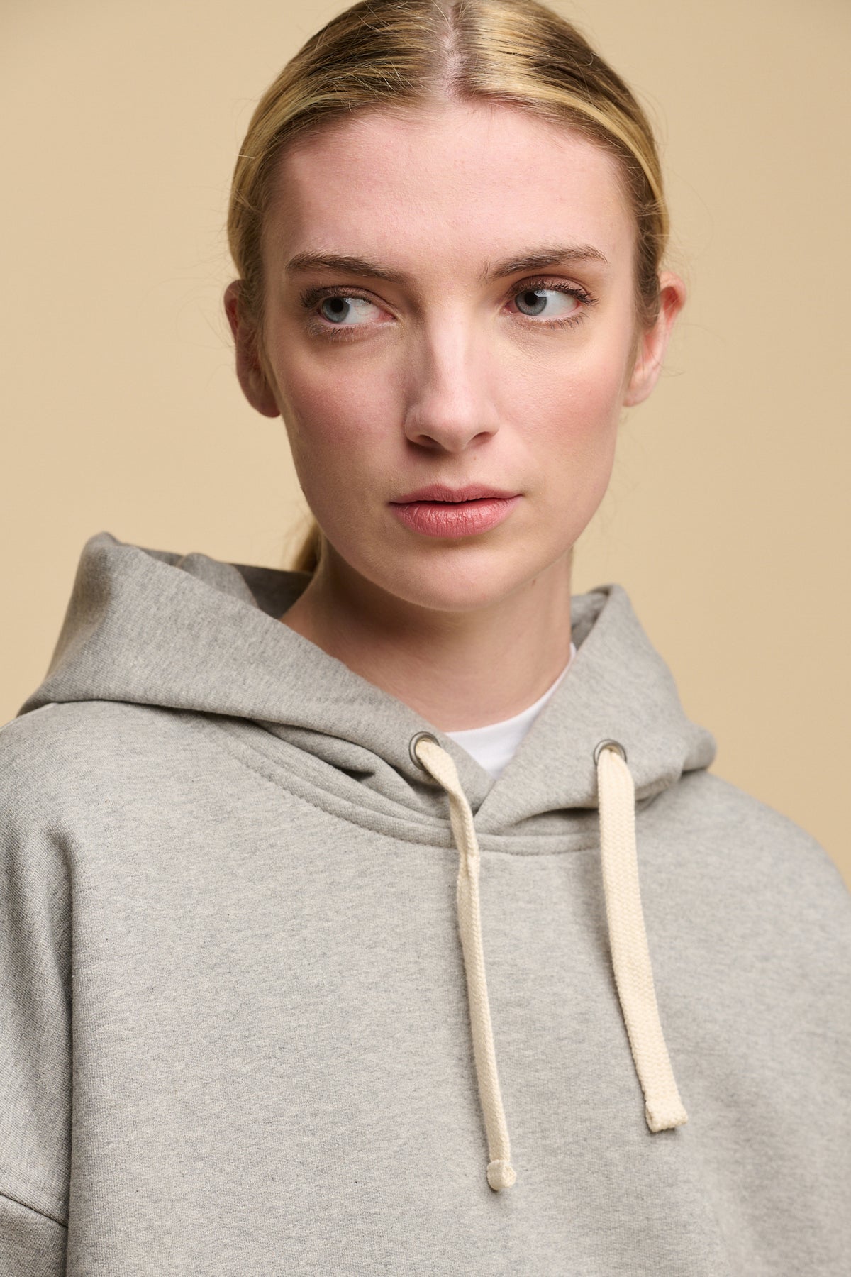 Portrait of female wearing heritage hooded sweatshirt in grey worn over crew neck t shirt in white. Ecru drawstring through the hood
