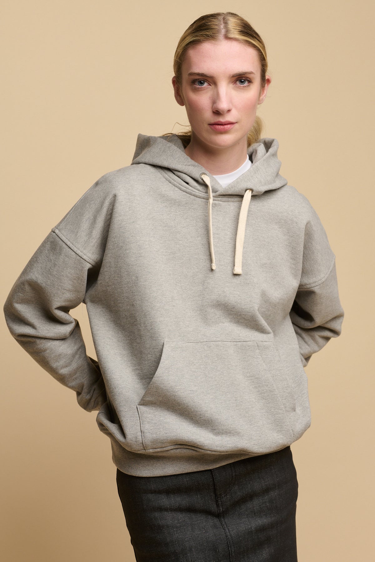 Female with blonde hair wearing heritage hooded sweatshirt in grey with ecru drawstring through the hood. worn over crew neck white t shirt in white