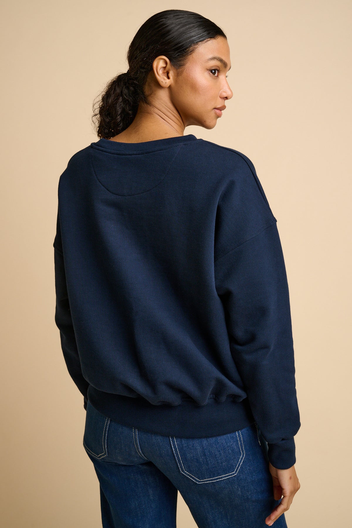 Woman wearing a navy blue sweatshirt and blue jeans against a beige background