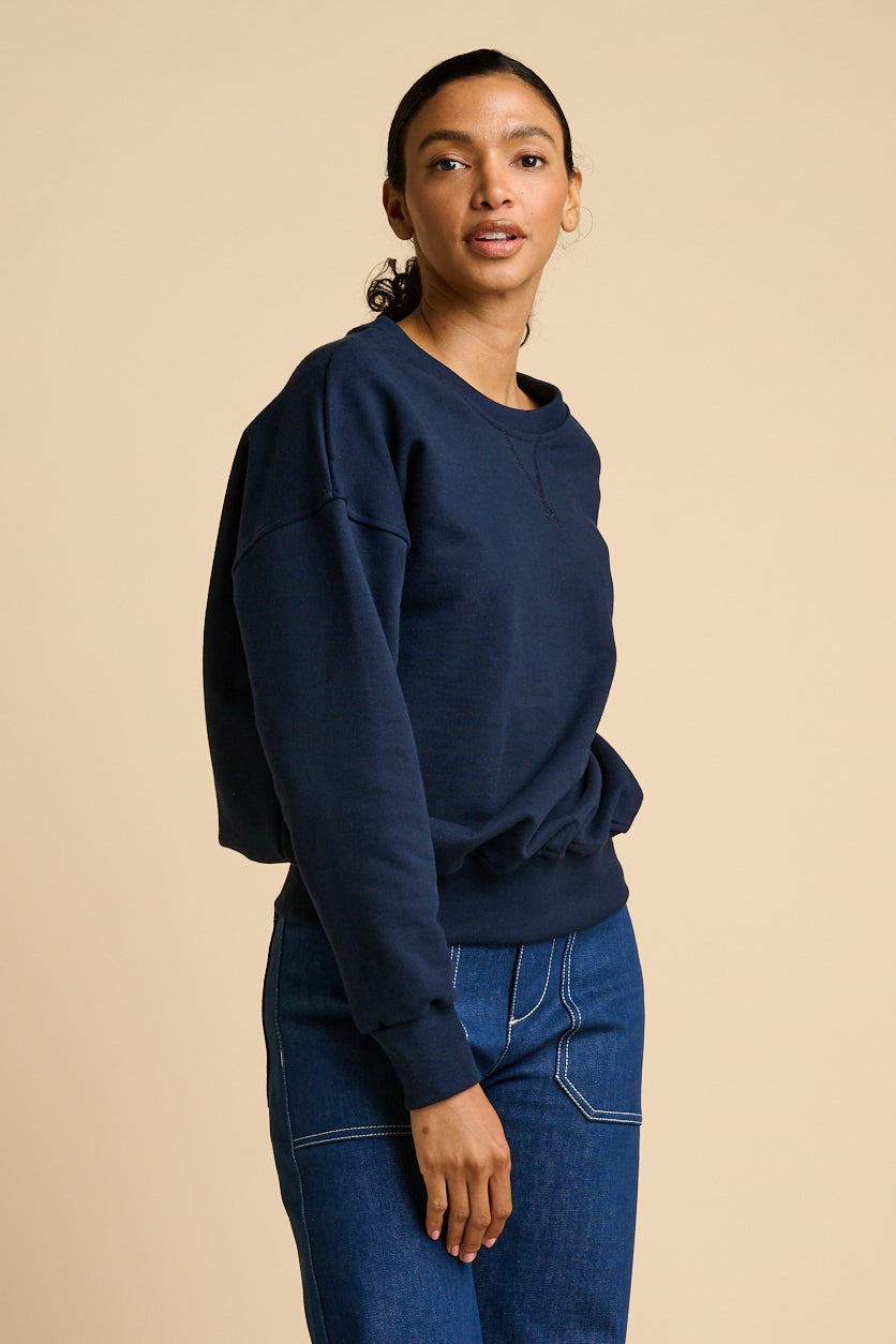 Woman wearing a navy blue sweatshirt and blue jeans against a beige background