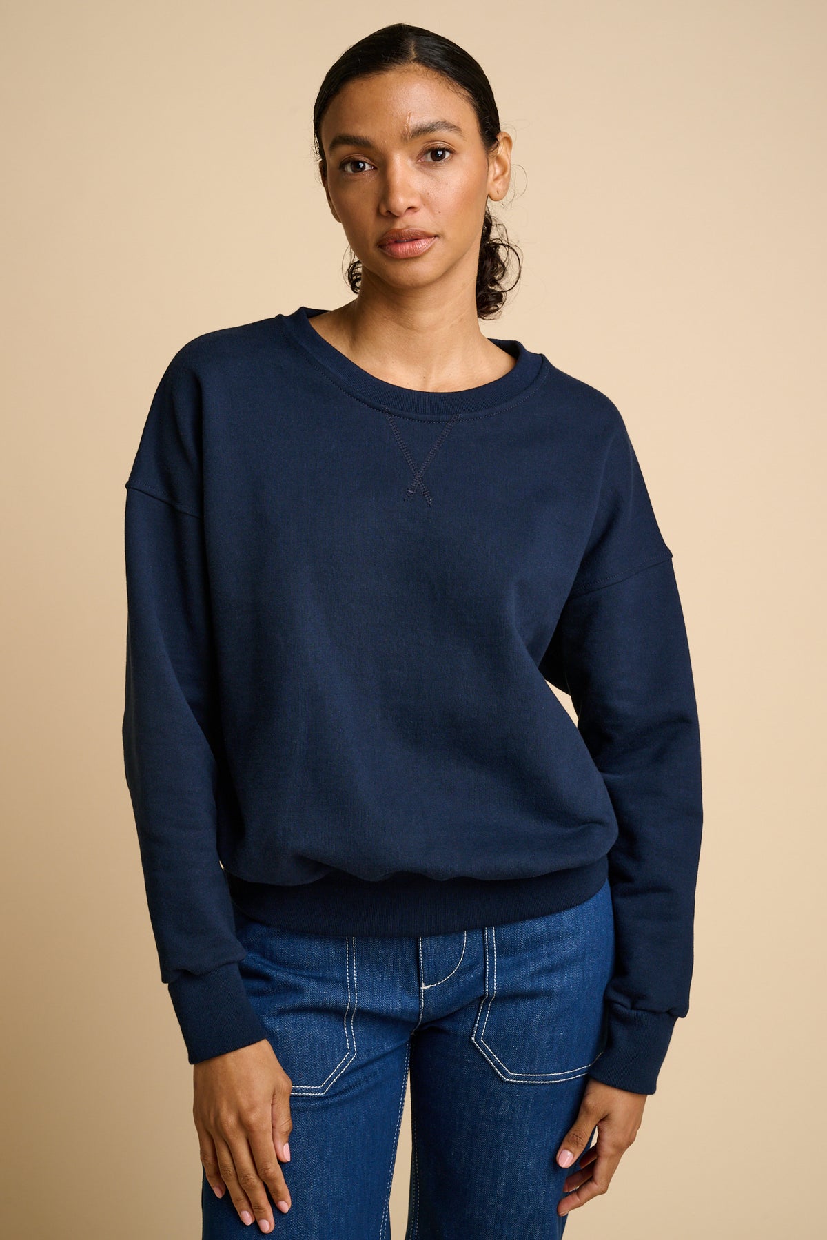 Woman wearing a navy blue sweatshirt and blue jeans against a beige background
