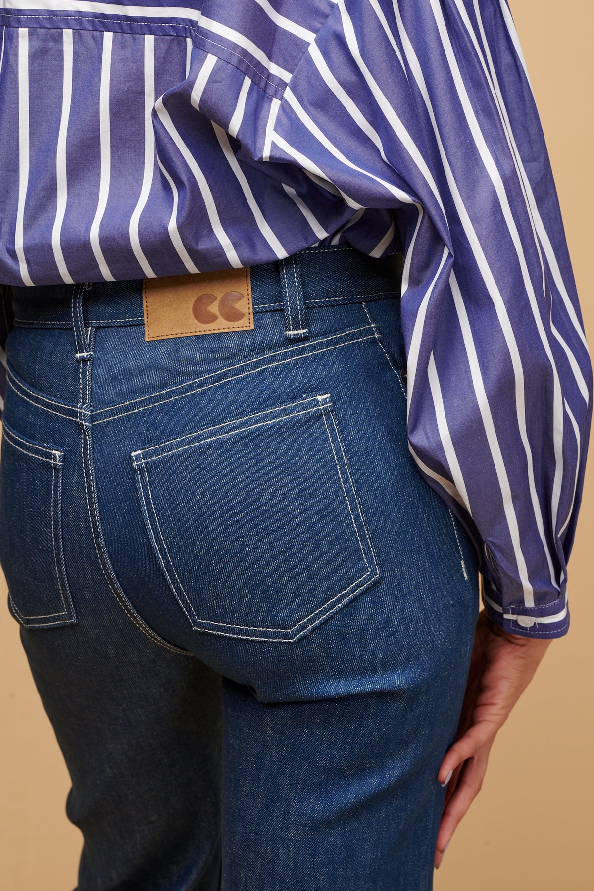 Close up of the back of high rise wide leg jeans in blue with two back pockets and brown jeans patch with CC logo on waistband with belt loops