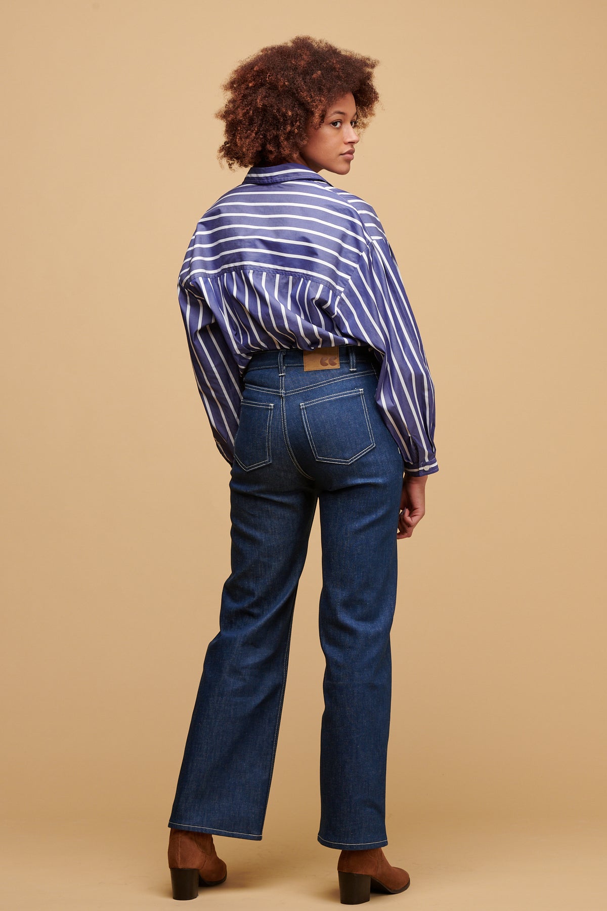 
            The back of female wearing high rise wide leg jean in blue with Esme shirt in blue and white stripe tucked in