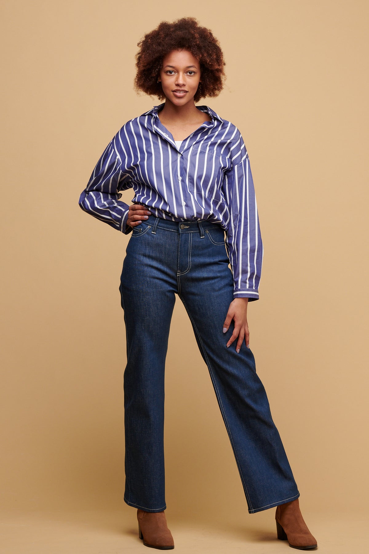 Black female wearing high rise wide leg jean in blue with Esme shirt in blue and white stripes tucked in paired with suede boots