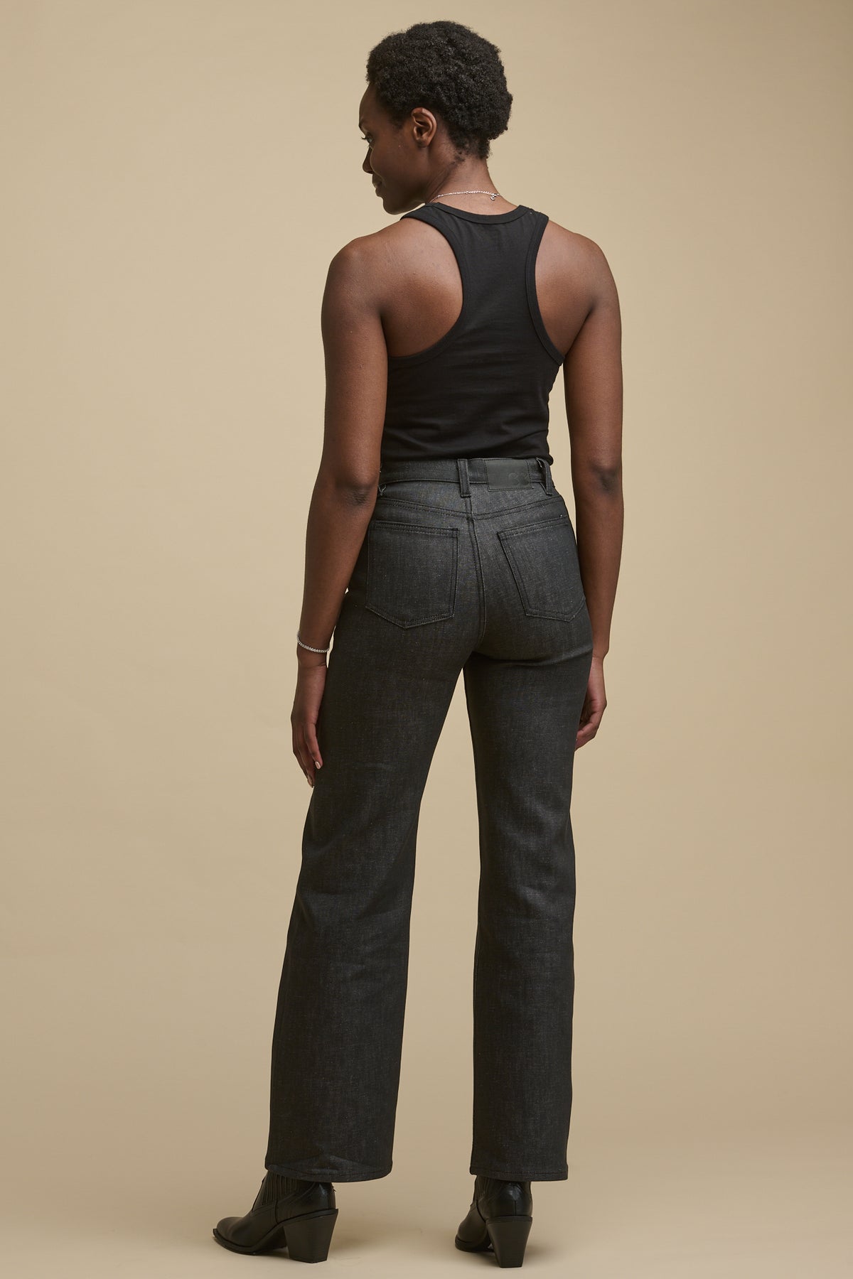 
            The back of female wearing high rise jeans in black paired with racer back vest in black tucked in