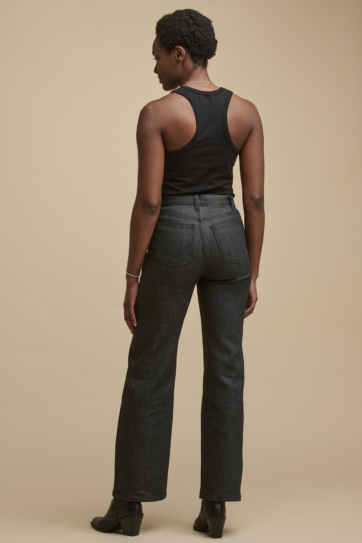 The back of female wearing high rise jeans in black paired with racer back vest in black tucked in