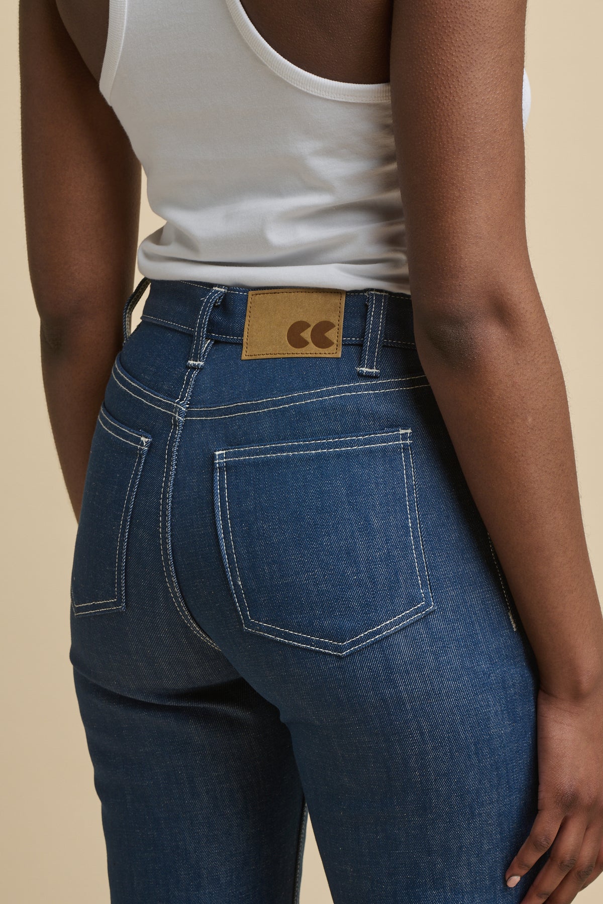 
            Close up image of the back of female wearing high rise wide leg jeans in blue with CC logo patch 