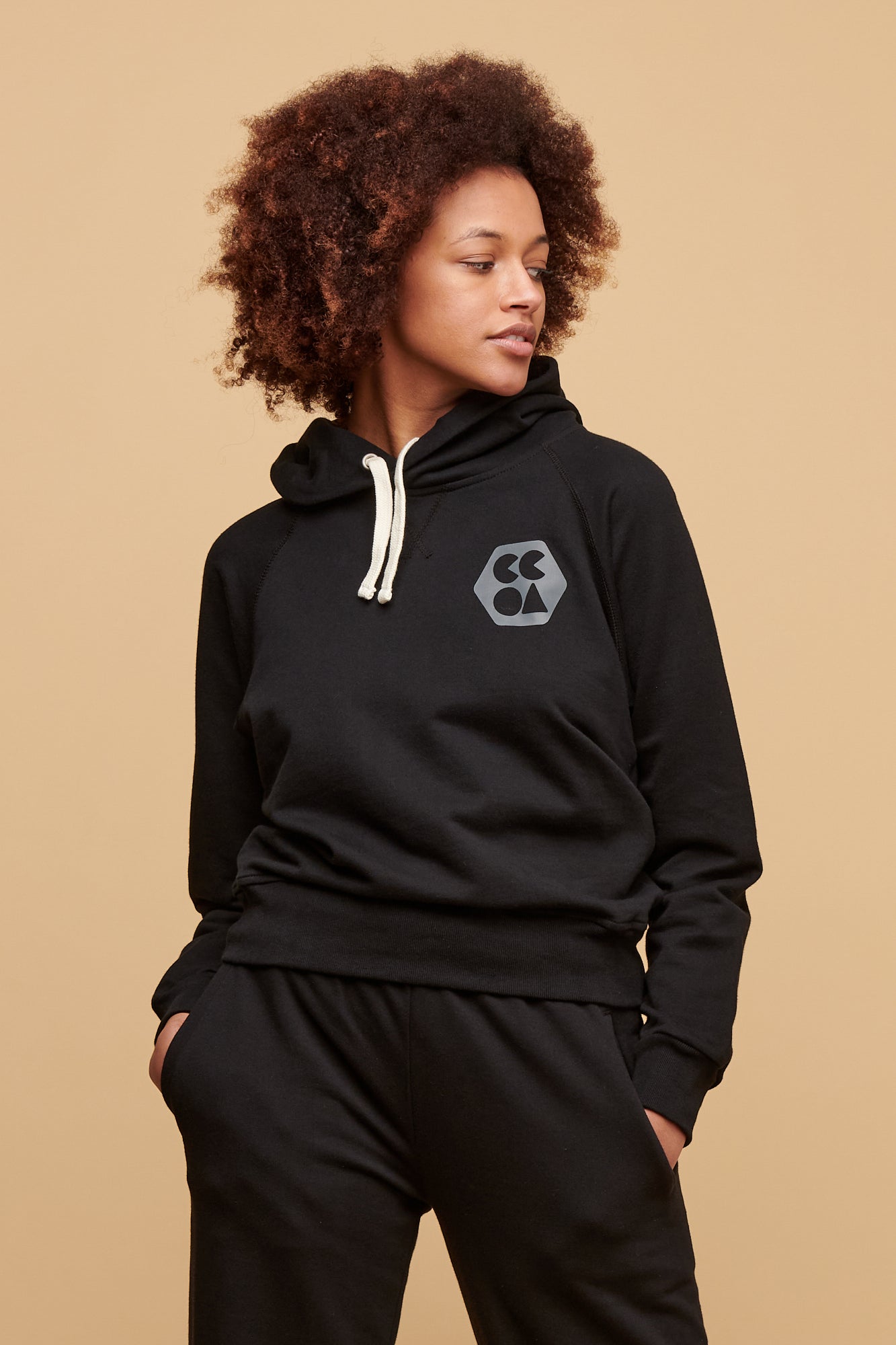 Thigh up of female wearing plastic free sweatshirt in black with CCOA logo print on the left of chest paired with 100% cotton sweatpants in black