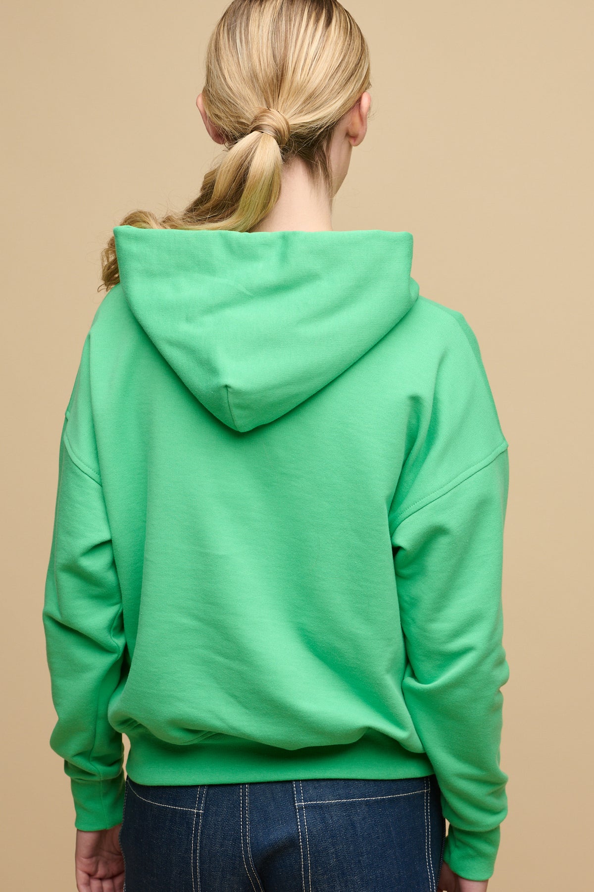 Thigh up image of the back of female wearing hooded sweatshirt in apple green