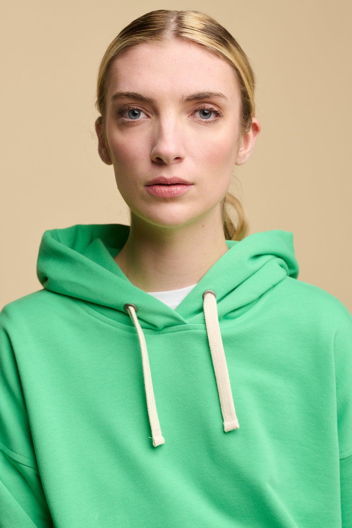 Portrait of Female wearing hooded sweatshirt in apple green over crew neck white t shirt. Ecru drawcord through the hood.