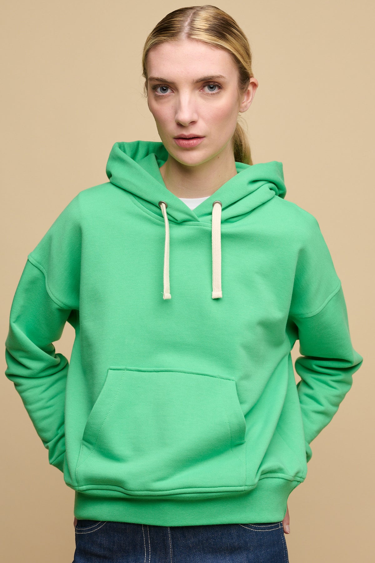 
            Thigh up image of female wearing hooded sweatshirt in apple green worn over white crew neck t shirt with blue jeans.