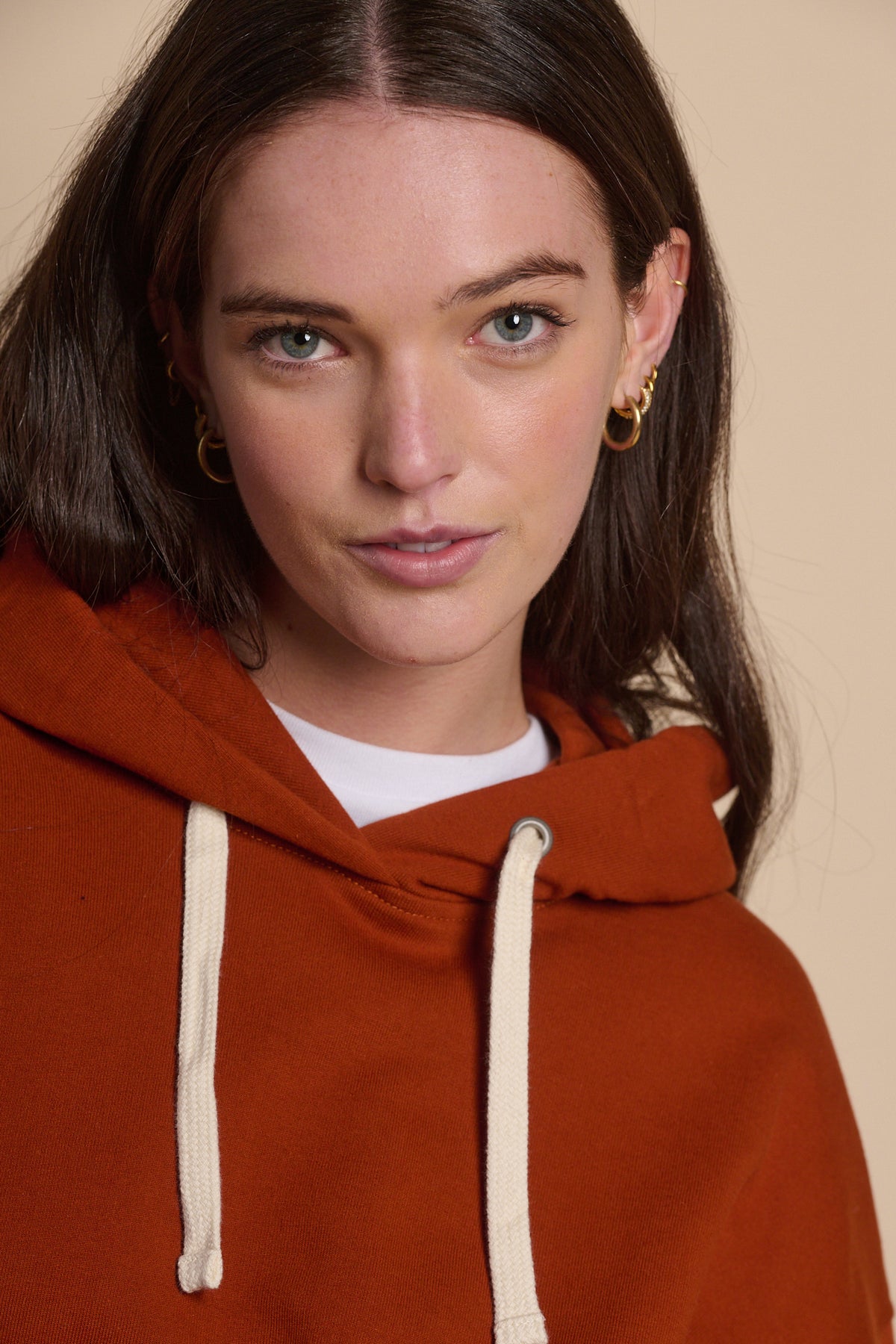 Portrait of white female with brunette hair showing ecru drawcord on the hood of hooded sweatshirt in cinnamon