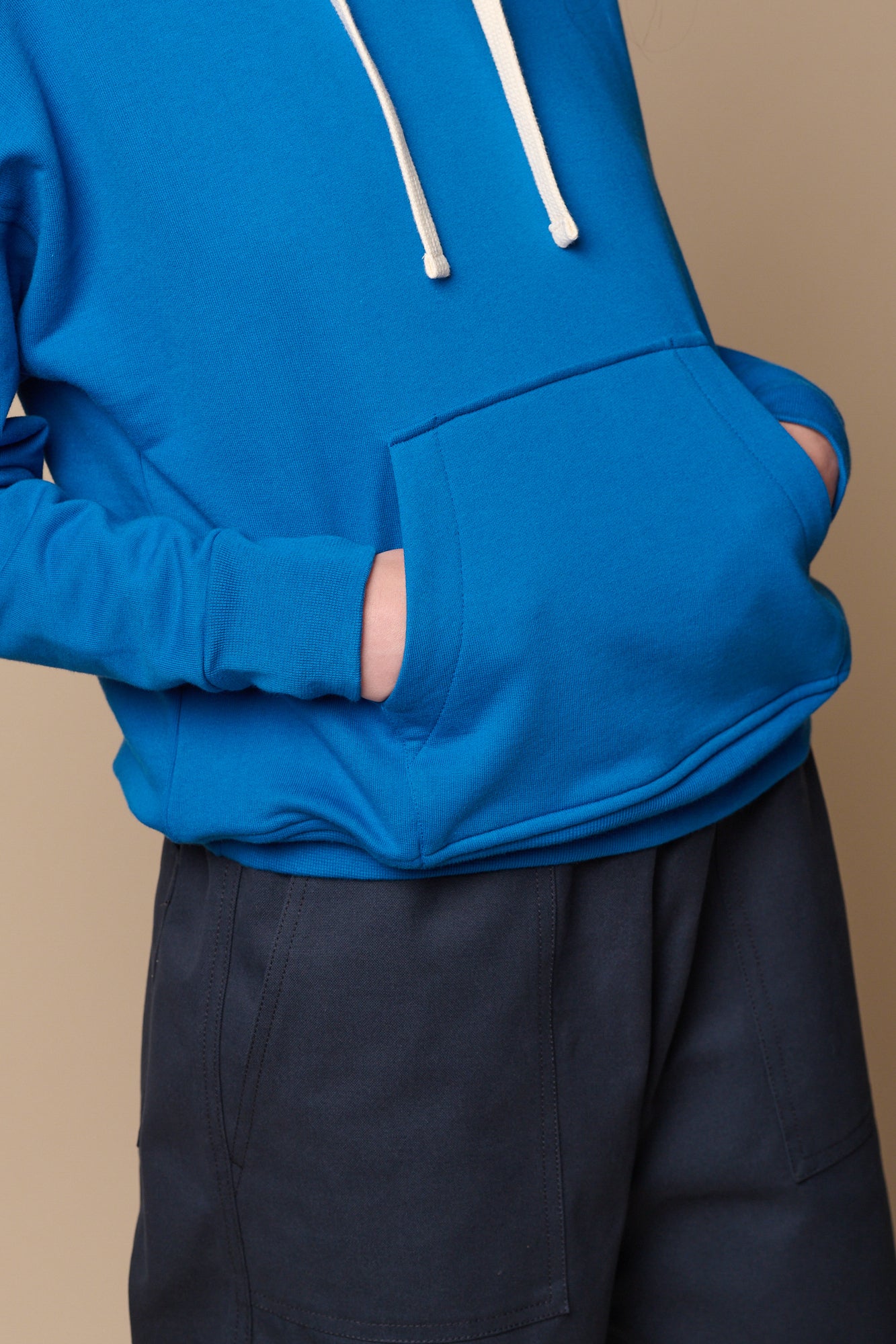 ecru drawcord detail of the hood, model has both hands in large, front central pocket