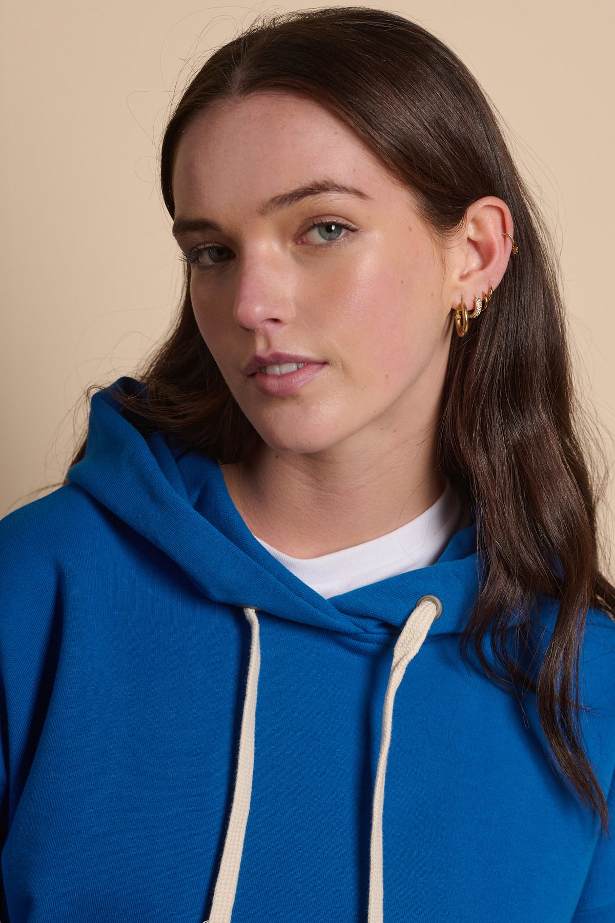 Portrait of brunette female wearing hooded sweatshirt in cobalt. ecru drawstring through the hood