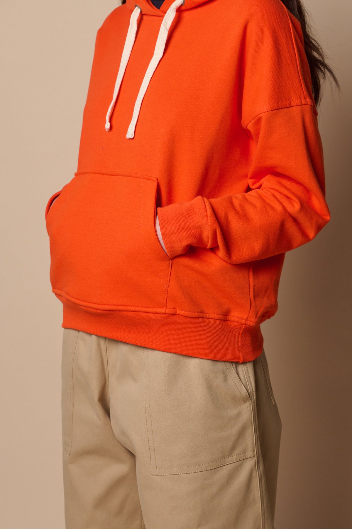 Thigh up image of female wearing hooded sweatshirt in flame red with hands in front pocket.