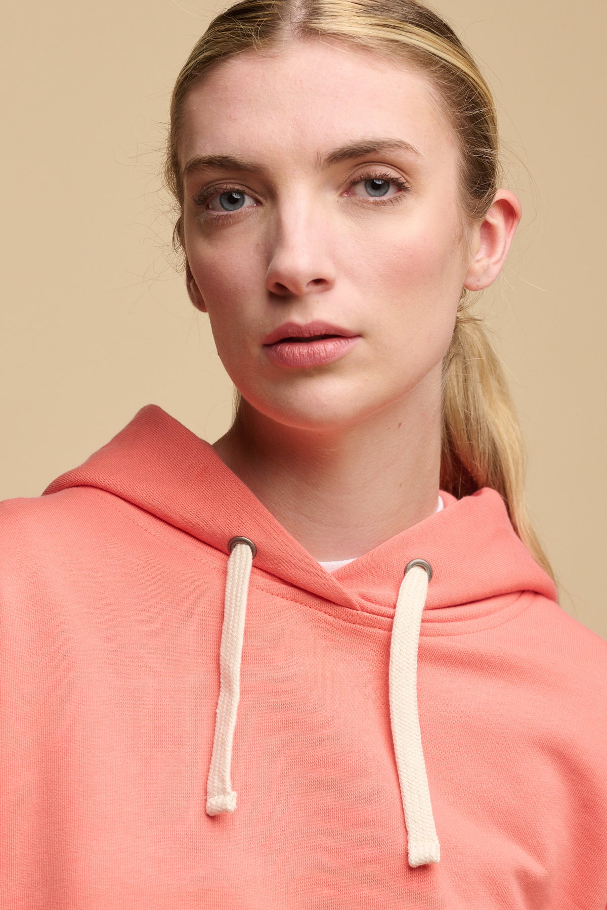 
            Portrait of female wearing hooded sweatshirt in peach with ecru drawstring through the hood