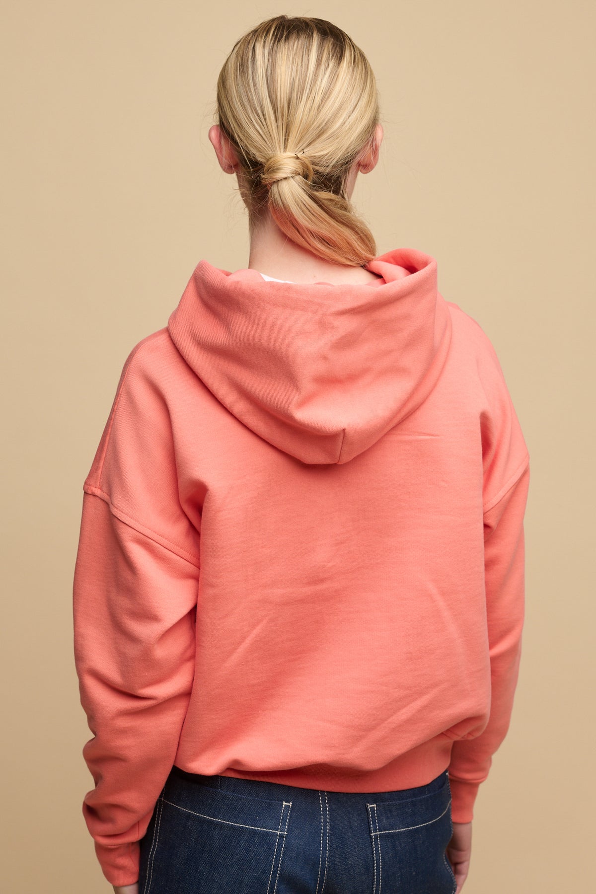 
            Hip up of the back of female wearing hooded sweatshirt in peach paired with work jeans in blue