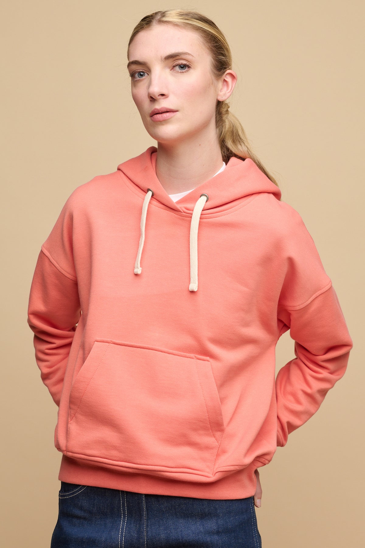 
            Hip up image of female wearing hooded sweatshirt in peach with hands on back of hips