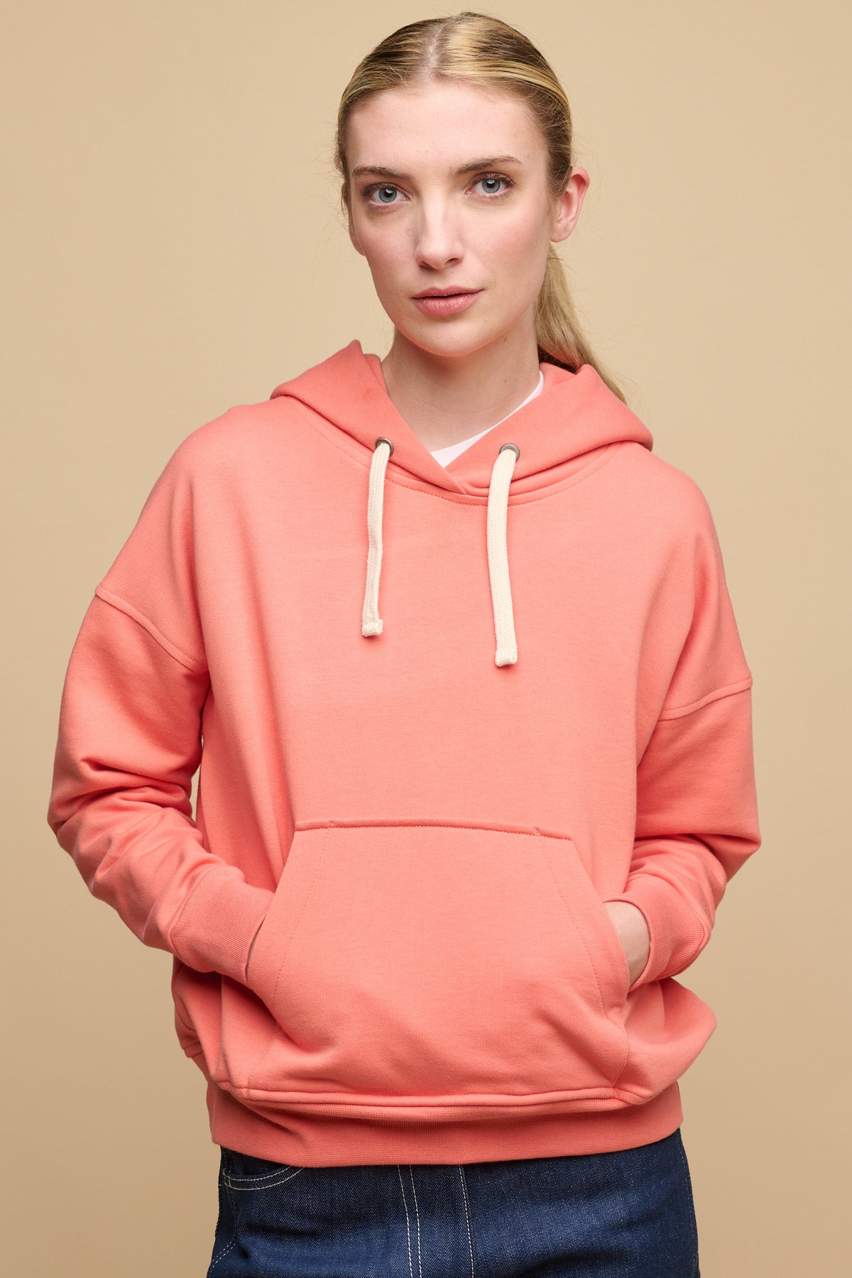 
            Hip up image of female wearing hooded sweatshirt in peach with hands in front pocket of hooded sweatshirt in peach