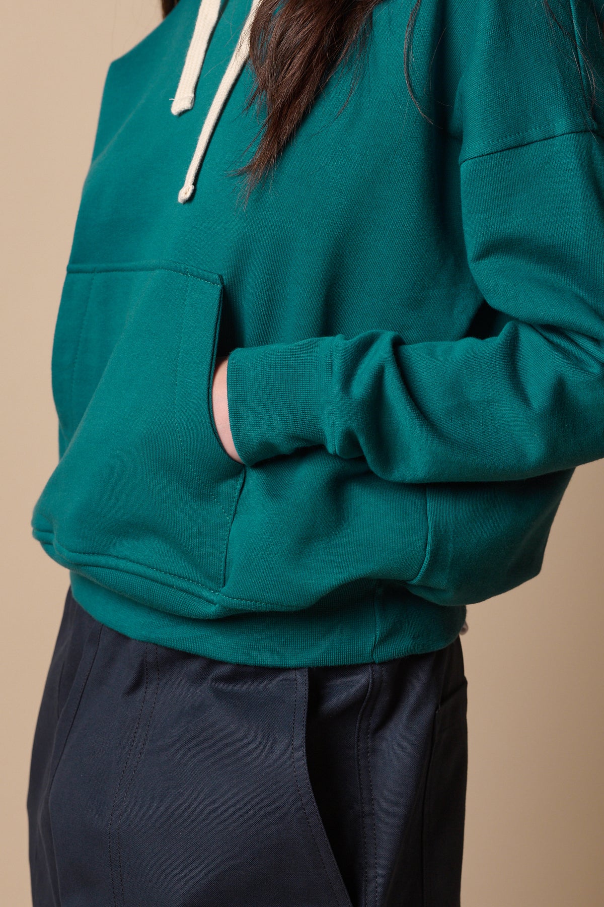 Close up image of model with hand in front pocket of hooded sweatshirt in teal