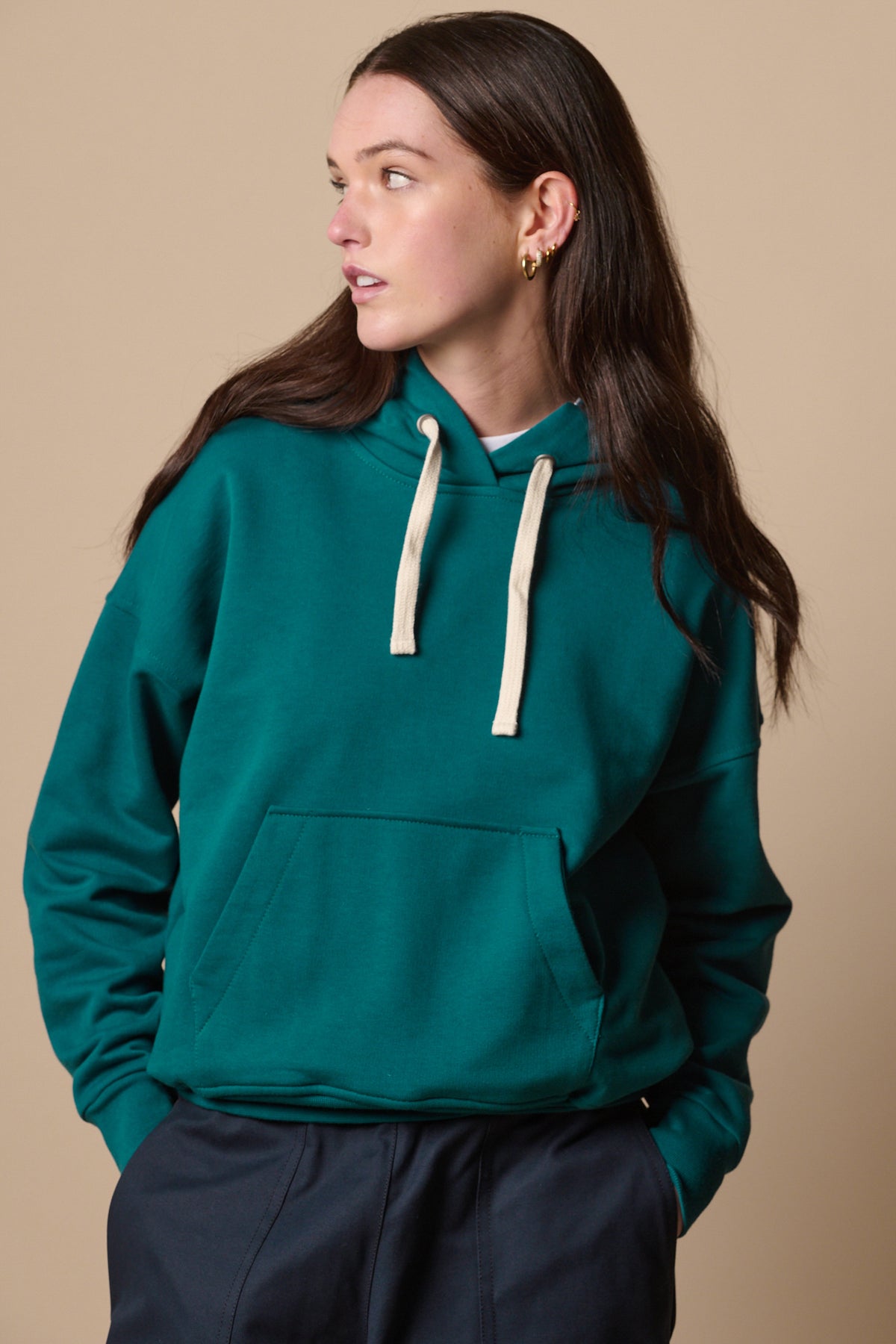 White female wearing hooded sweatshirt in teal, ecru drawcord for hood