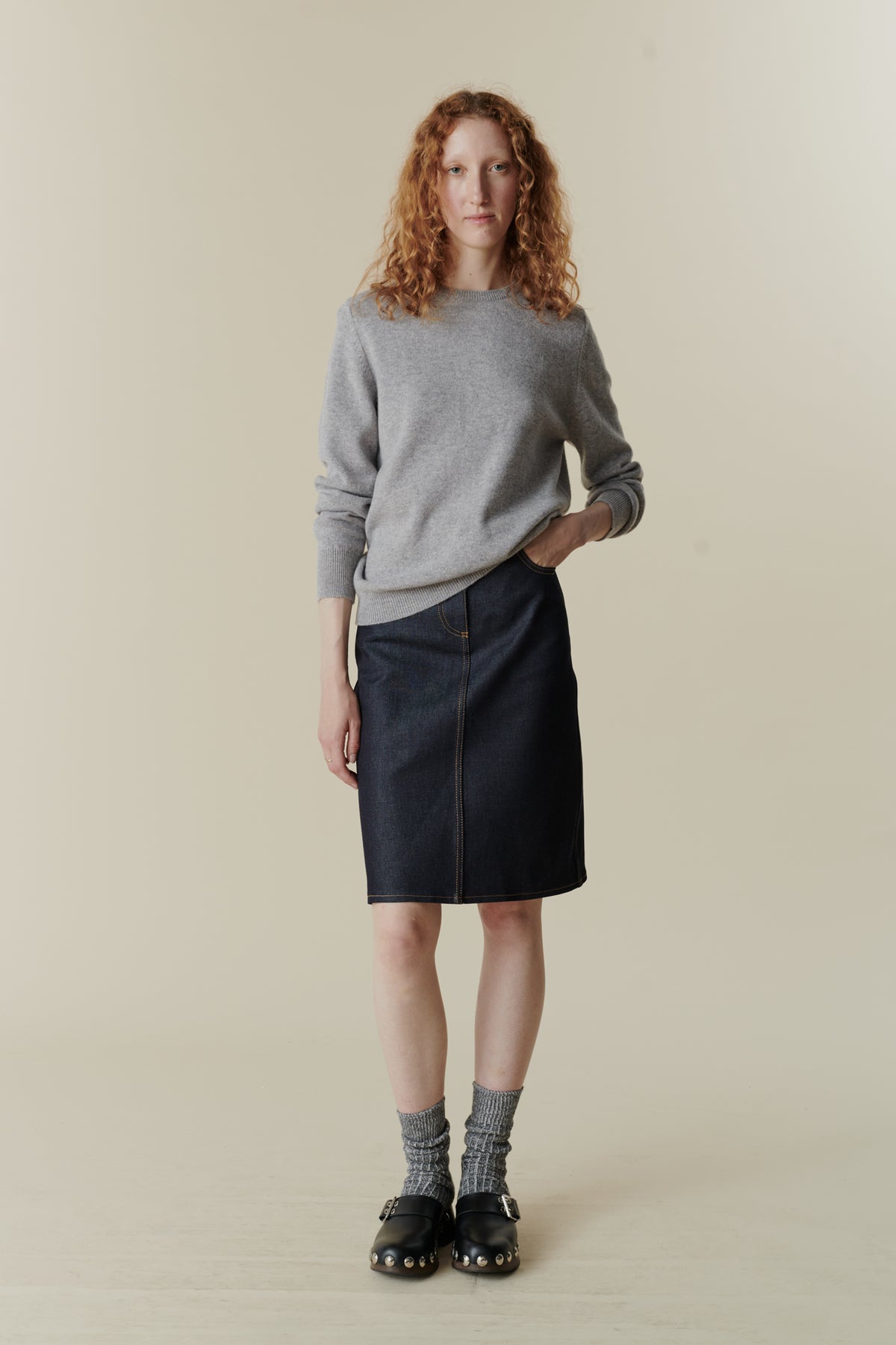 Female wearing knee length jean skirt in indigo denim with front pockets. Worn with women's lambswool crew neck jumper in light grey.
