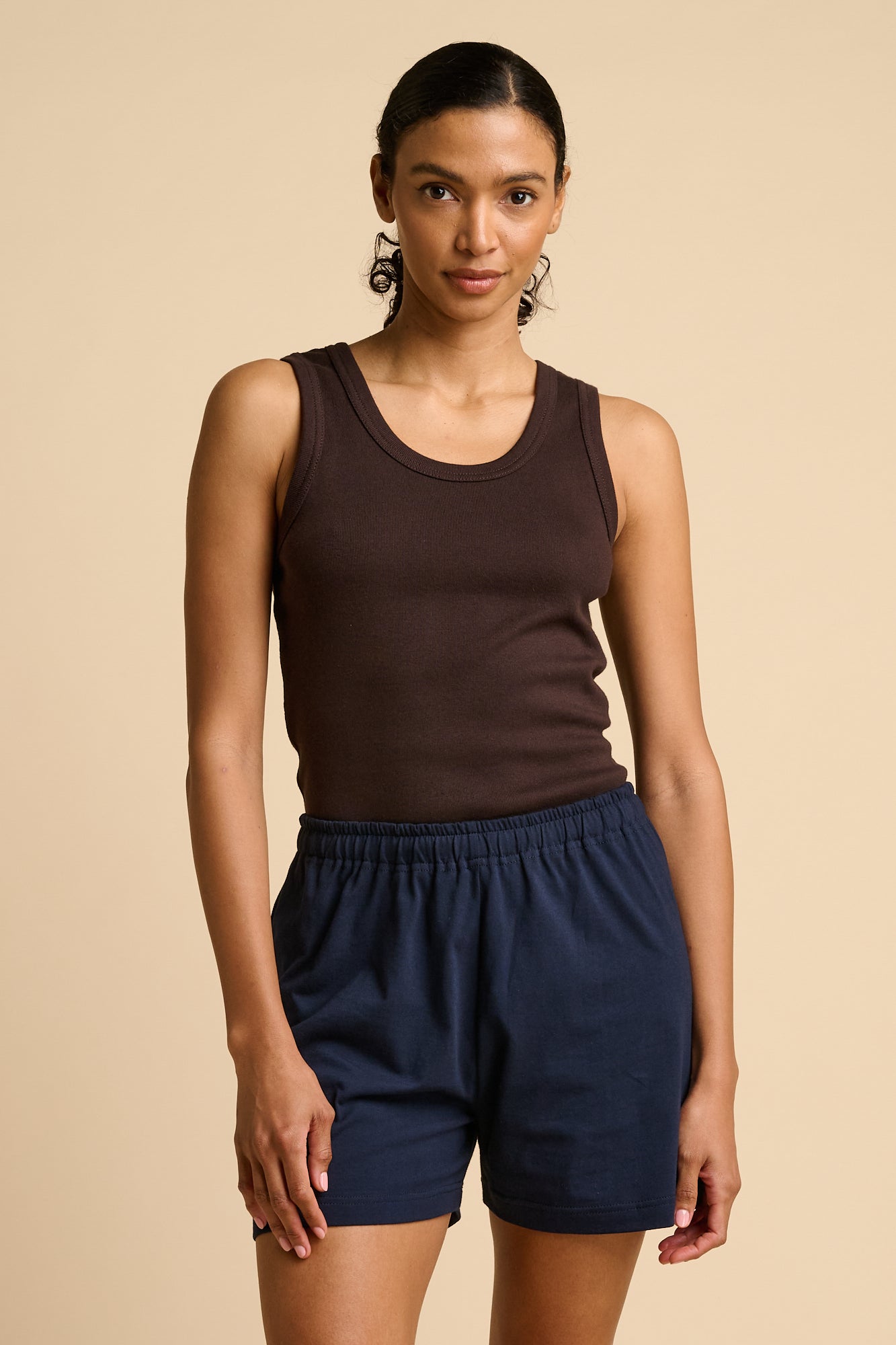 Woman wearing a brown tank top and navy shorts on a beige background