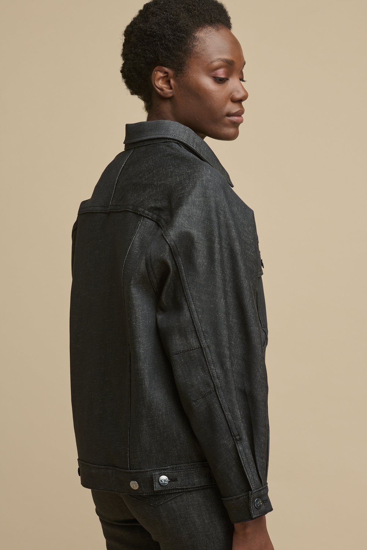 
            Thighup image of the back of black female wearing Jodie denim jacket in black with adjustable button fastenings on the hem