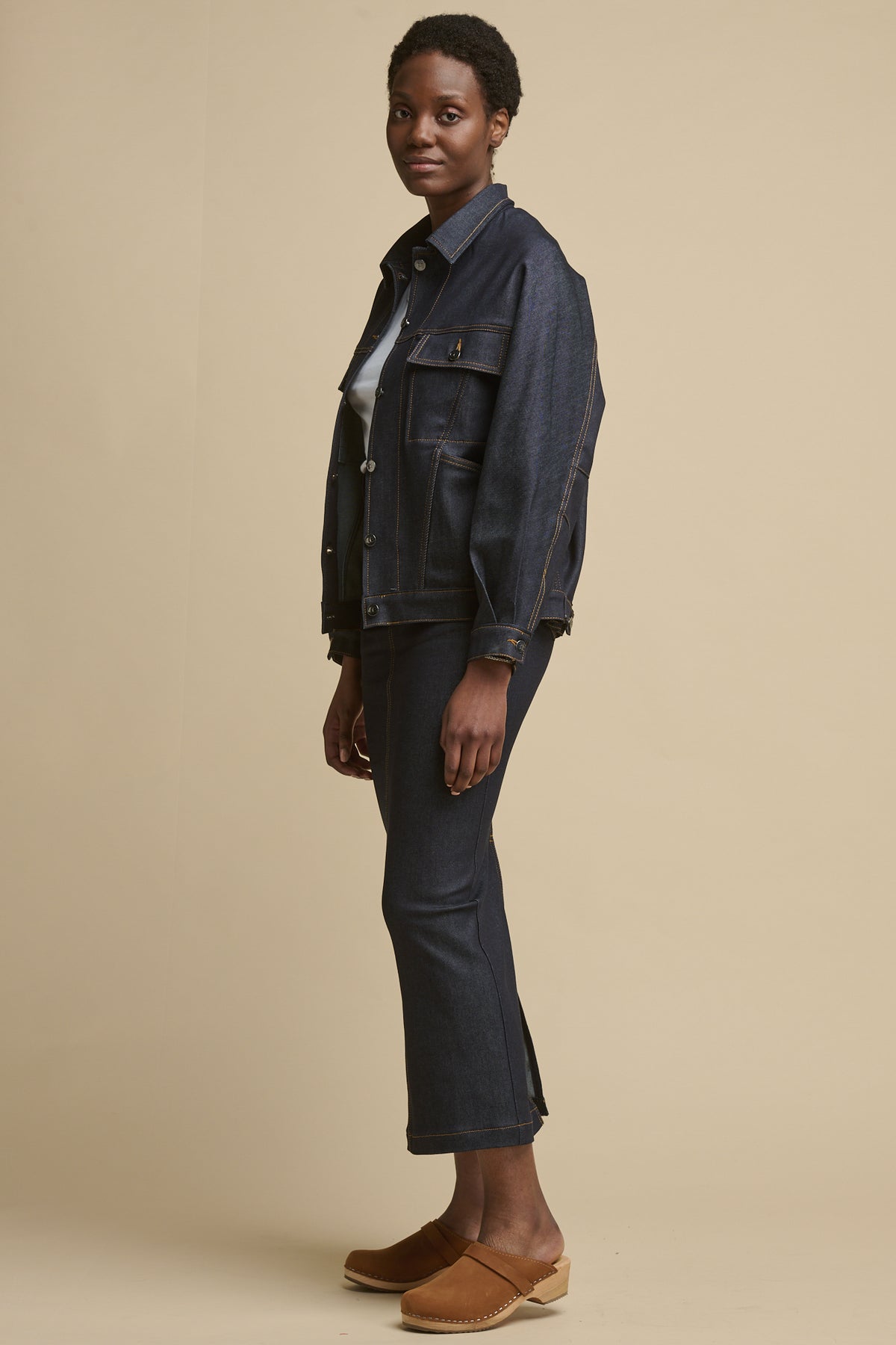 
            Full body image of the side of female wearing Jodie denim jacket in indigo denim showing button fastening cuff paired with Frankie maxi skirt in indigo denim