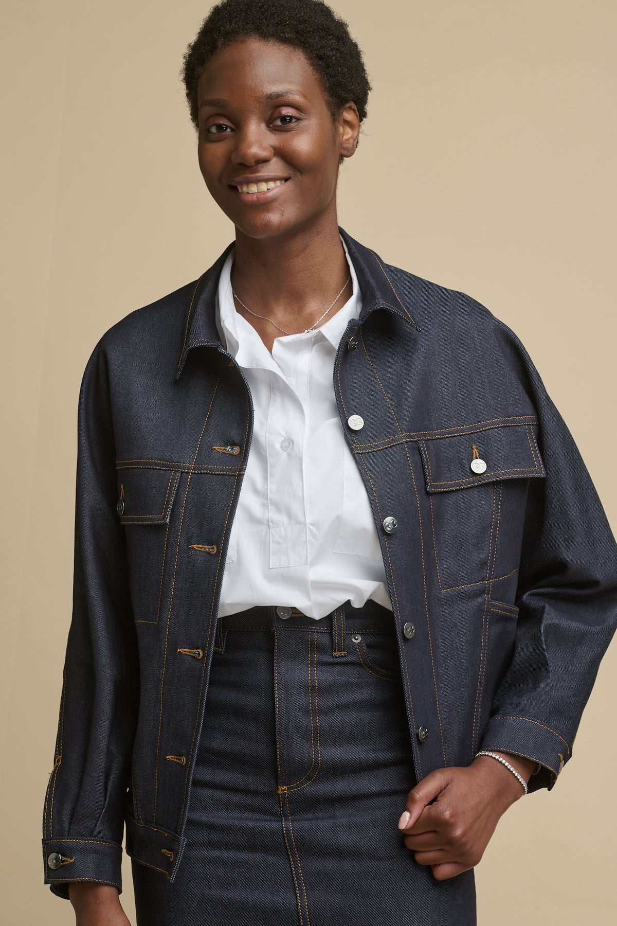 Thigh up image of smiley female wearing Jodie denim jacket in indigo with two front chest pockets with flats