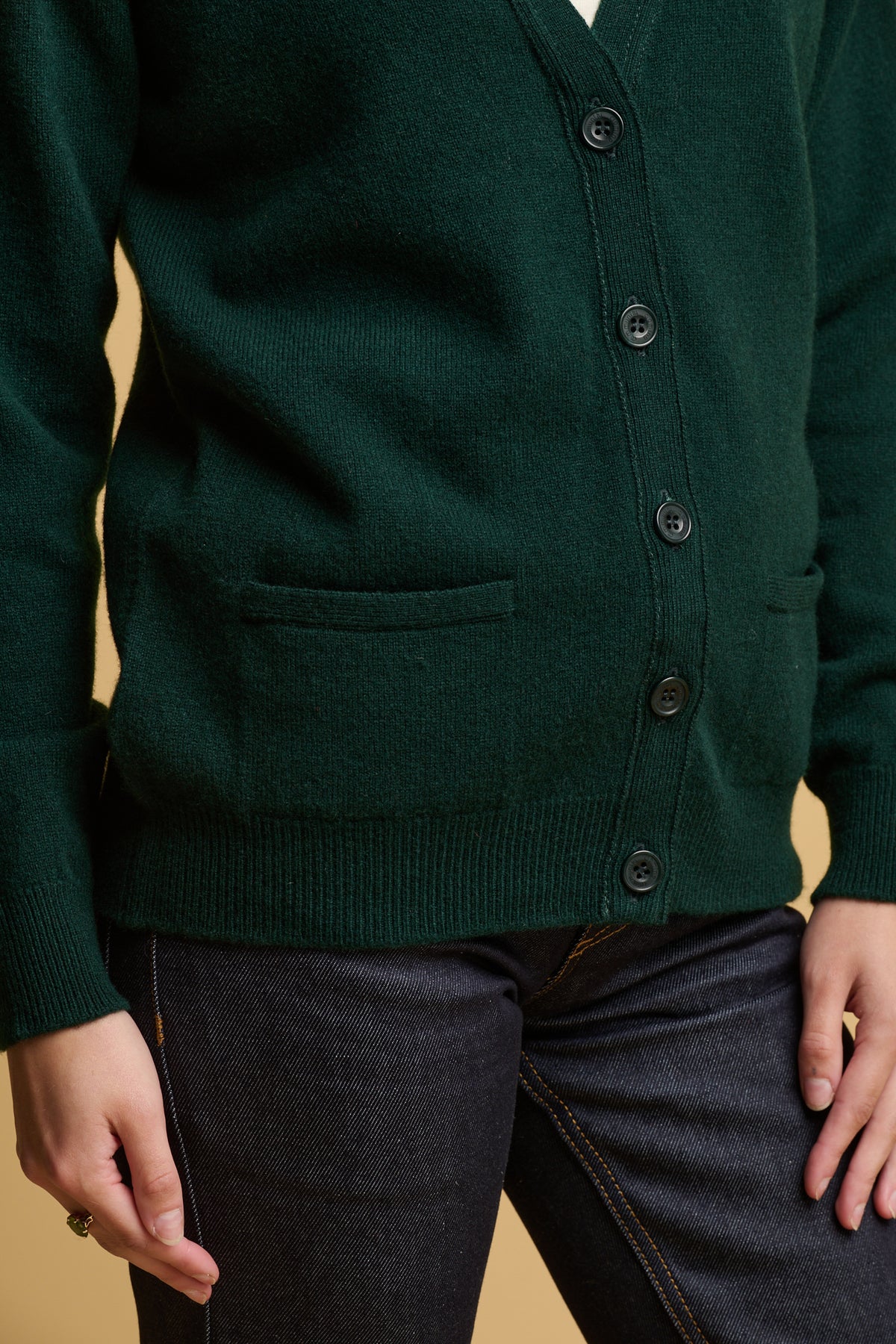 
            Close up shot of buttoned up lambswool cardigan in bottle green with two front pockets