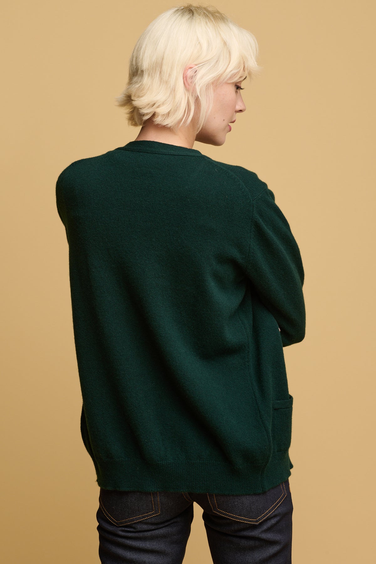 
            Thigh up of the back of female wearing lambswool cardigan in bottle green  worn with straight leg jeans in indigo